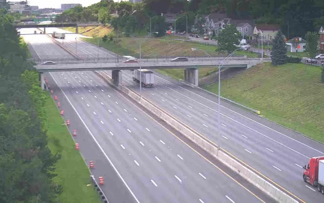 Wide highway with several lanes and an overpass, trucks traveling in both directions, flanked by grassy slopes and trees. I-70 Closed June 19 - Oliver Law Office