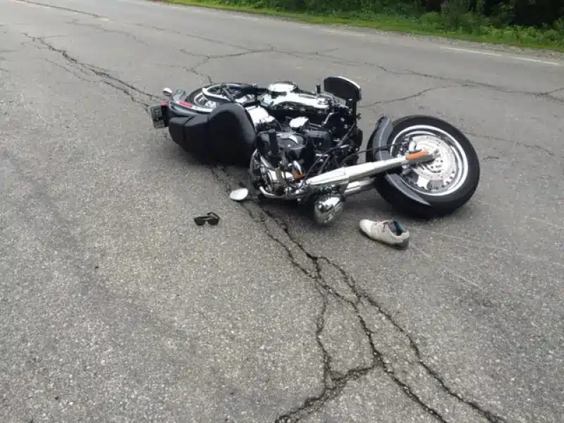 Black motorcycle on its side in the middle of a cracked road after a crash; a shoe and a helmet lie nearby. Motorcycle crash - Oliver Law Office