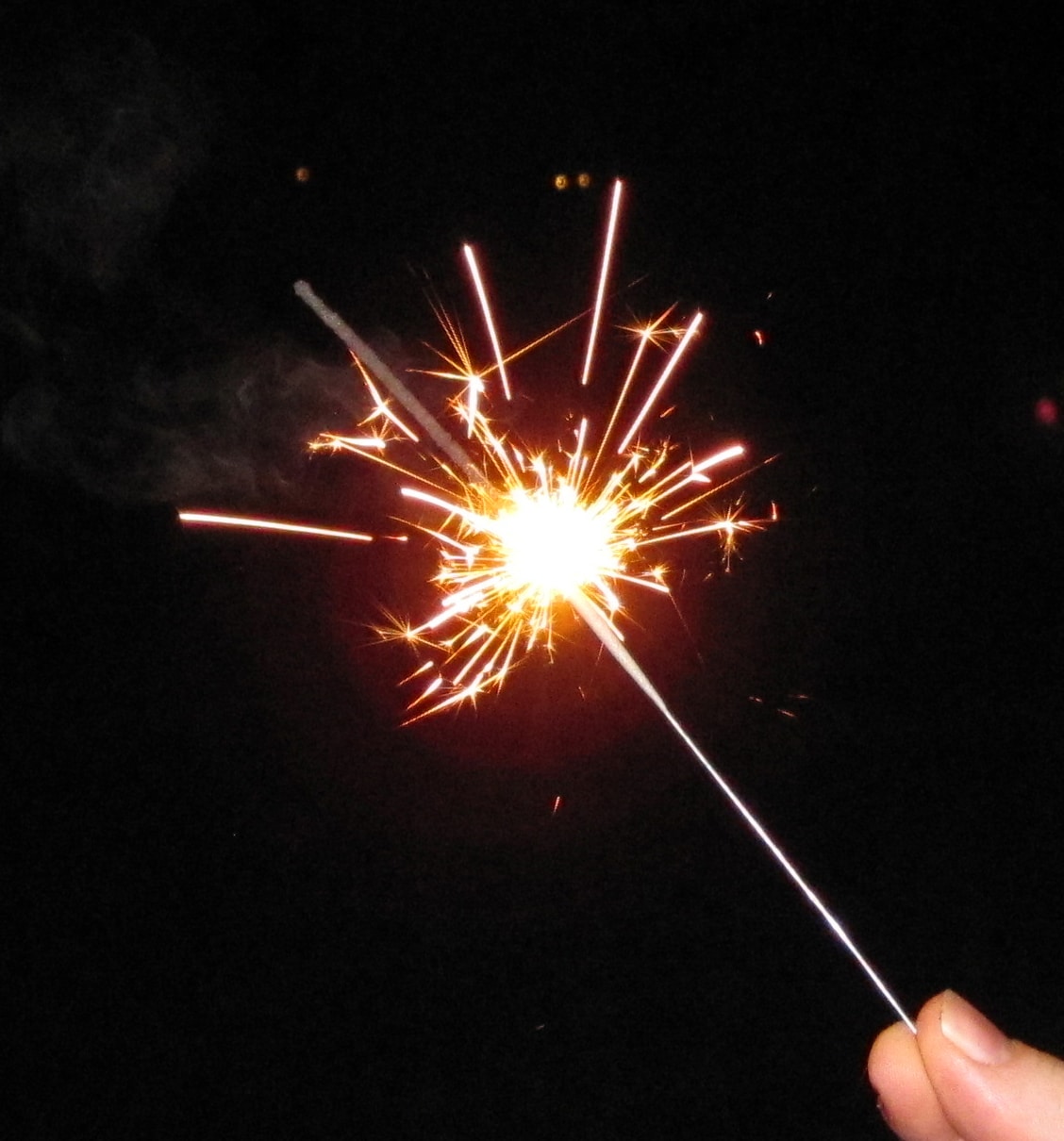 Hand holding a lit sparkler with bright orange-white sparks against a dark background. Sparkler - Oliver Law Office