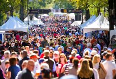Crowded street festival with white vendor tents and a dense crowd strolling between booths.