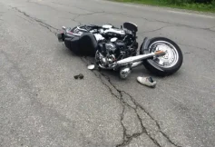 Black motorcycle on its side in the middle of a cracked road after a crash; a shoe and a helmet lie nearby.